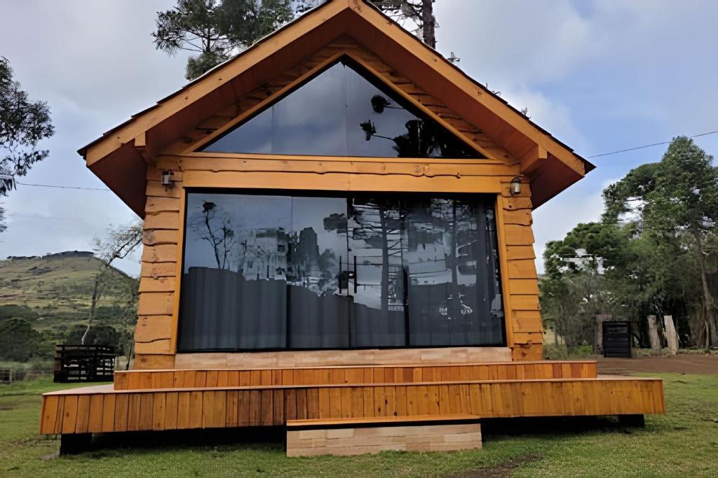 una pequeña casa con una gran ventana en el césped en Cabana Pequeno Bosque com deck e vista p/ o rio, en São Joaquim