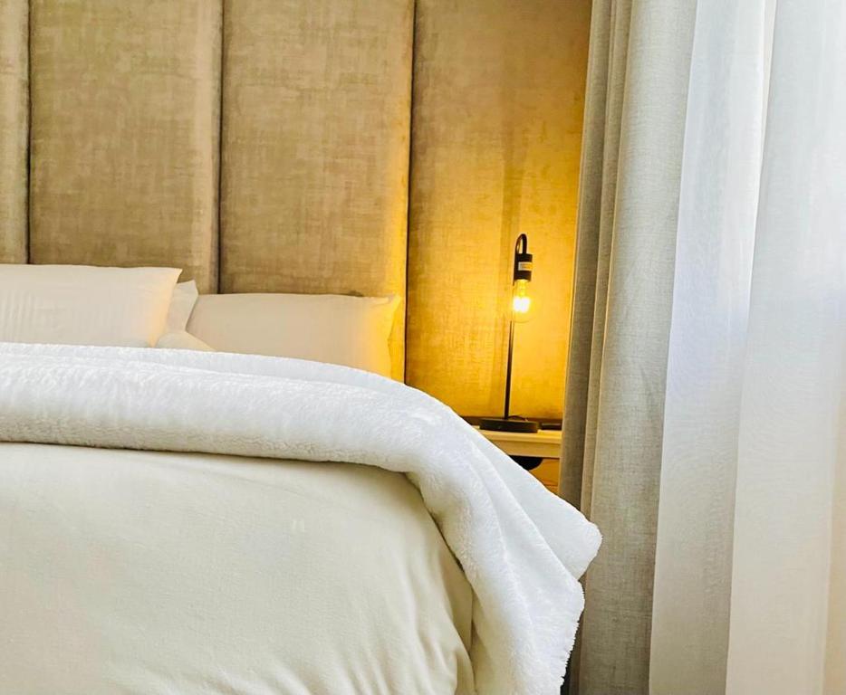 a bed with white sheets and a light next to a window at Tafre Hospitality @ Stratford, Menlyn in Pretoria
