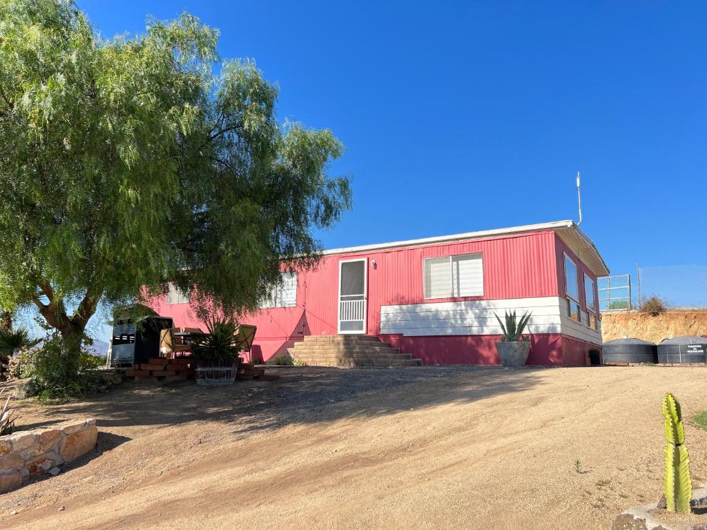 ein rotes Haus mit einem Baum davor in der Unterkunft Rancho Matalote en Valle de Guadalupe in Valle de Guadalupe