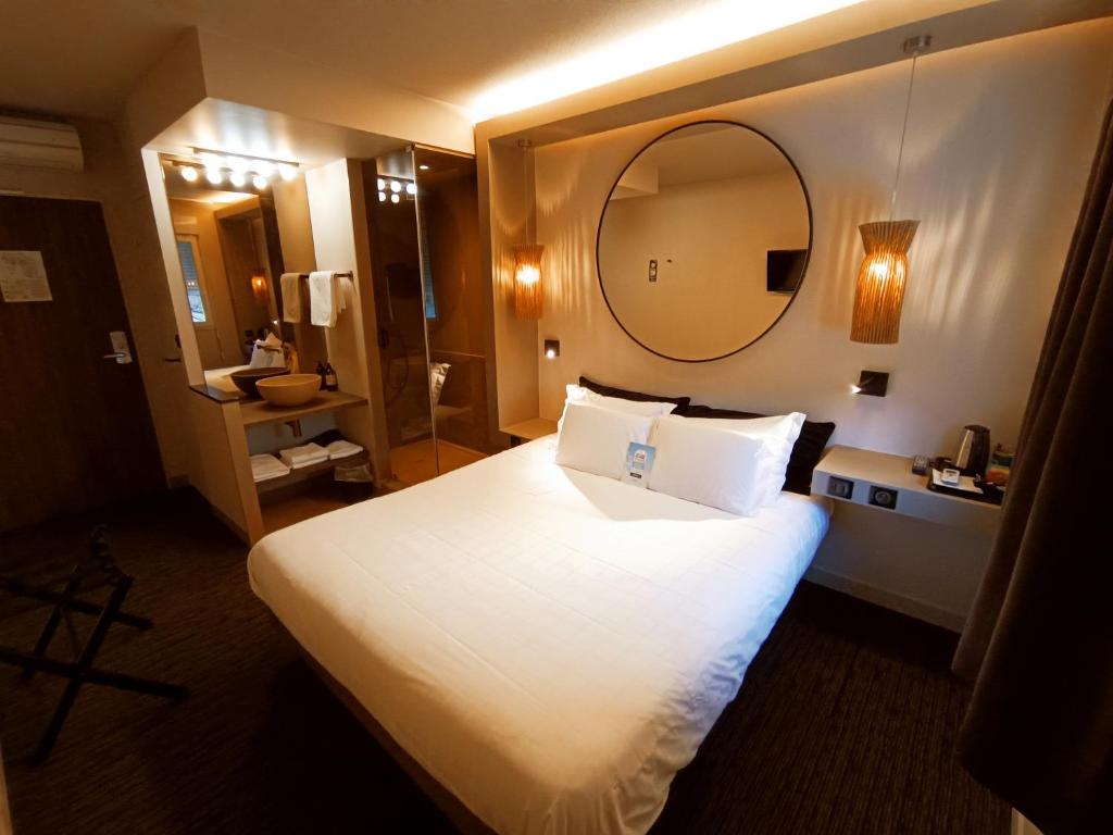 a hotel room with a large bed and a mirror at Hôtel Kyriad Brive Ouest in Brive-la-Gaillarde