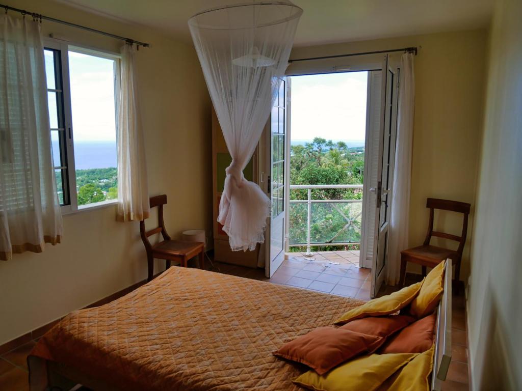 ein Schlafzimmer mit einem Bett und einem großen Fenster in der Unterkunft Appartement Emeraude et studio Azur in Gourbeyre