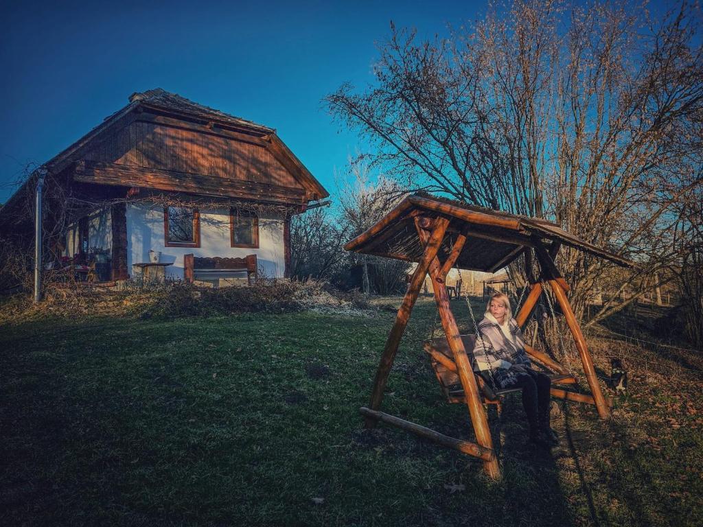 a woman sitting on a swing in front of a house at Fecskefészek Vendégház Őriszentpéter in Őriszentpéter