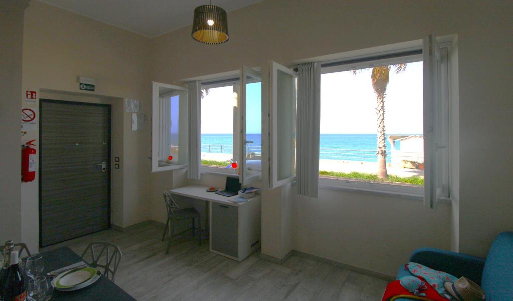 un soggiorno con scrivania e 2 finestre con vista sulla spiaggia di Capo d'Orlando Apartments - Doria 52 a Capo dʼOrlando