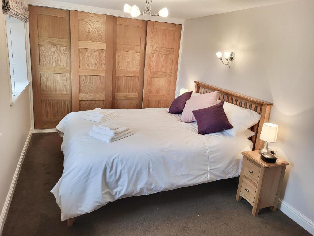 Schlafzimmer mit einem Bett mit weißer Bettwäsche und lila Kissen in der Unterkunft Grange Cottage in Aysgarth
