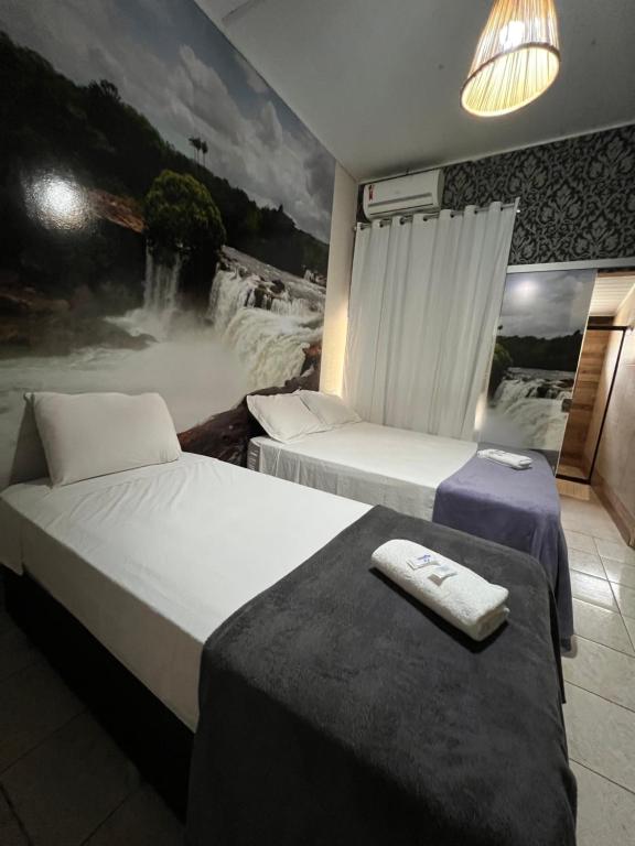 two beds in a room with a waterfall painting on the wall at POUSADA CABANA DO PARQUE in Mateiros