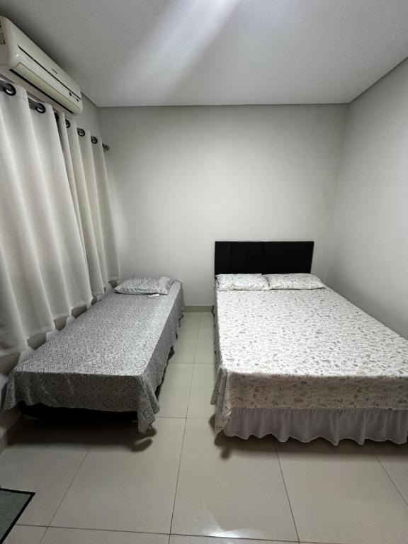 2 camas en una habitación con paredes y cortinas blancas en Casa 05 Dona D. PX A JK en Palmas