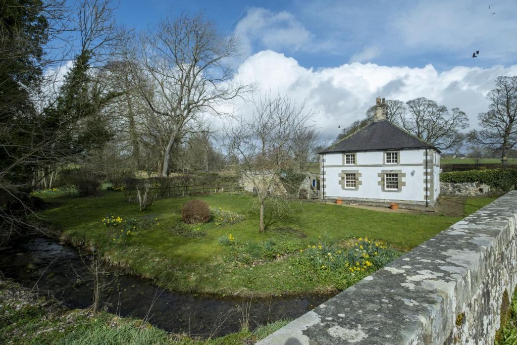uma casa branca com um jardim ao lado de uma parede de pedra em White Lodge Haughton Castle em Hexham