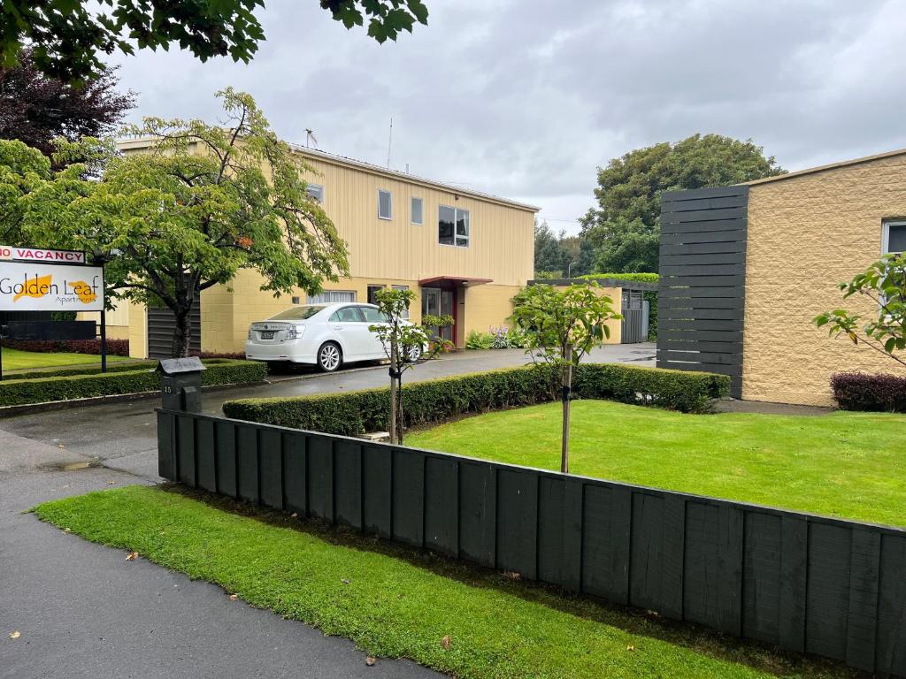 a fence in front of a building with a car at Golden Leaf Apartments in Invercargill