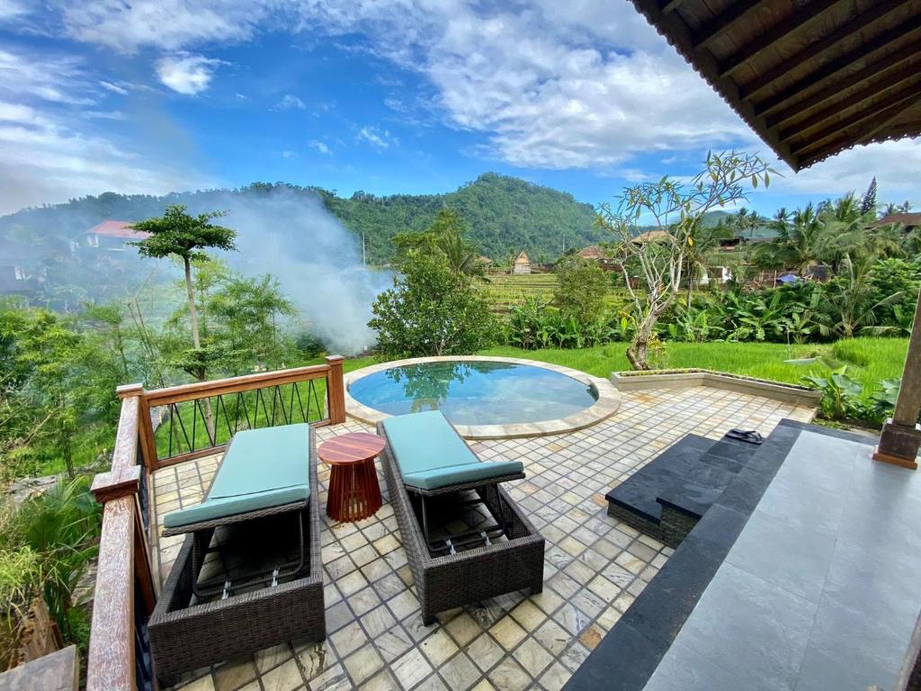 a patio with two chairs and a pool with mountains in the background at Abian Ayu Villa in Sidemen