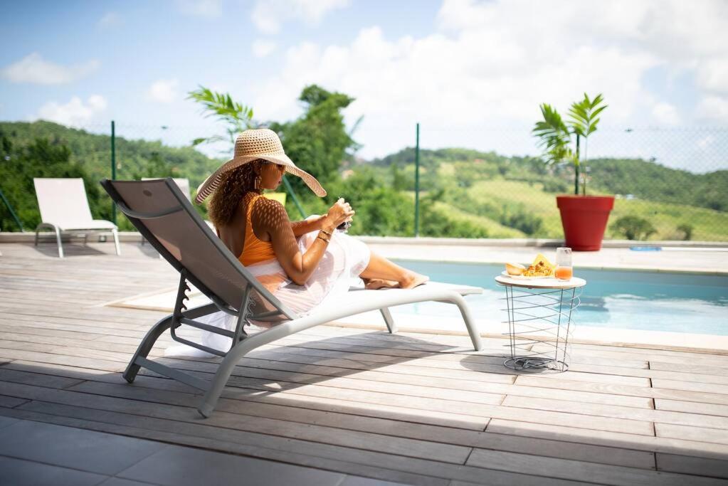 Eine Frau auf einem Stuhl neben einem Pool in der Unterkunft Séjour Glycéria: Villa Canne à Sucre in Le Marin