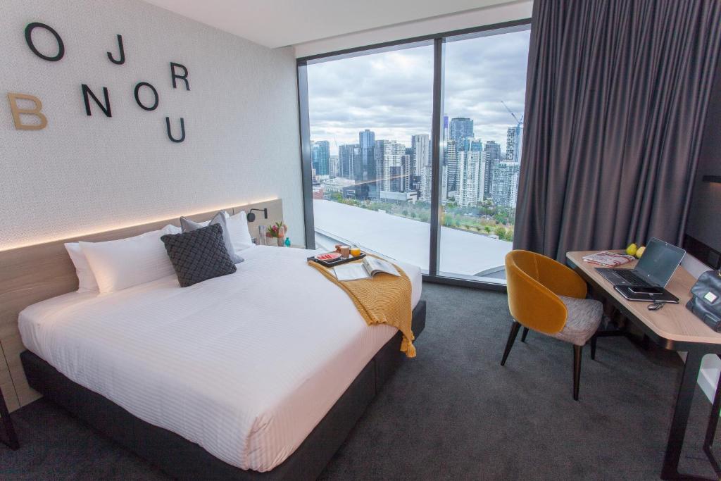 a hotel room with a bed and a desk and a window at Novotel Melbourne South Wharf in Melbourne