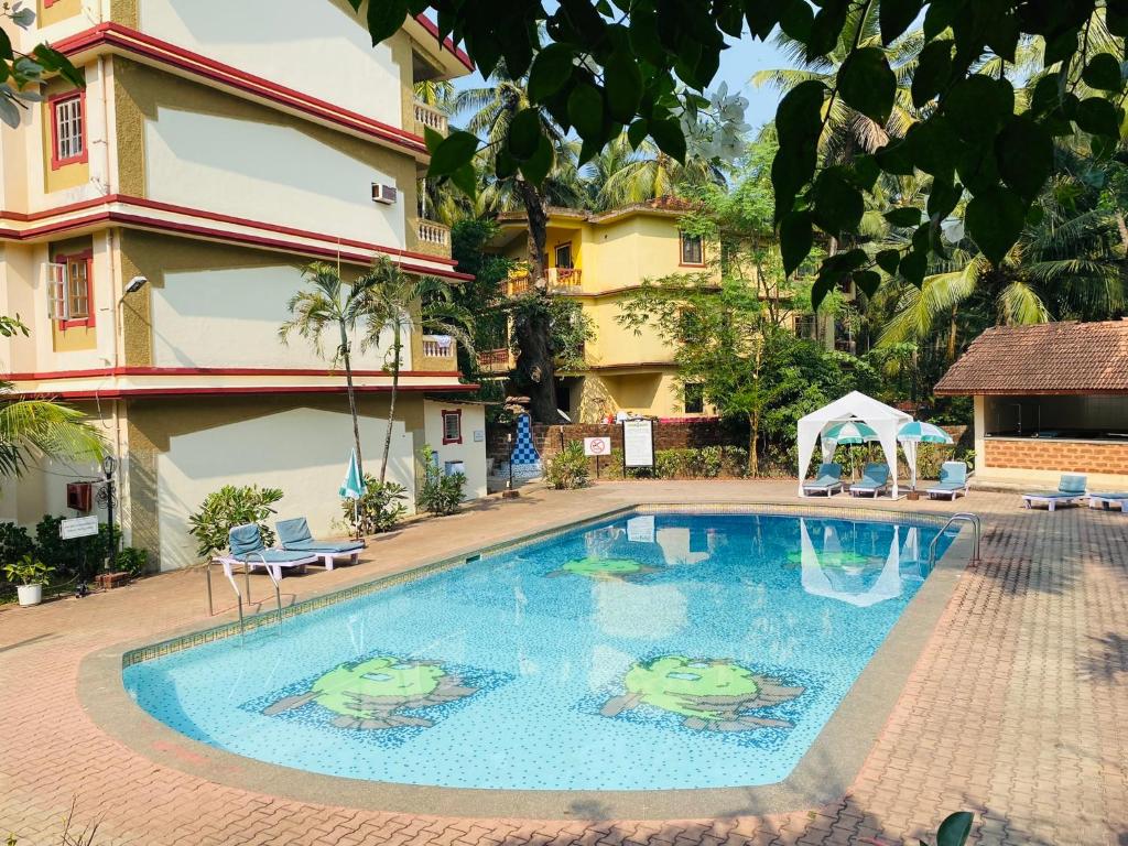 a swimming pool in front of a building with two frogs painted on it at Highland Beach Apartments Goa in Baga