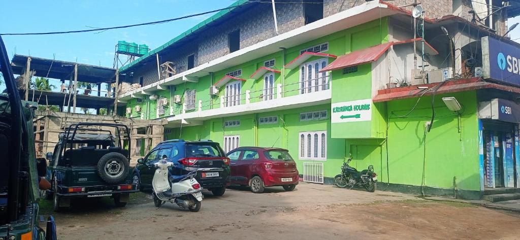 eine Gruppe von Autos, die vor einem grünen Gebäude geparkt werden in der Unterkunft Hotel Kaziranga Holidays in Kāziranga