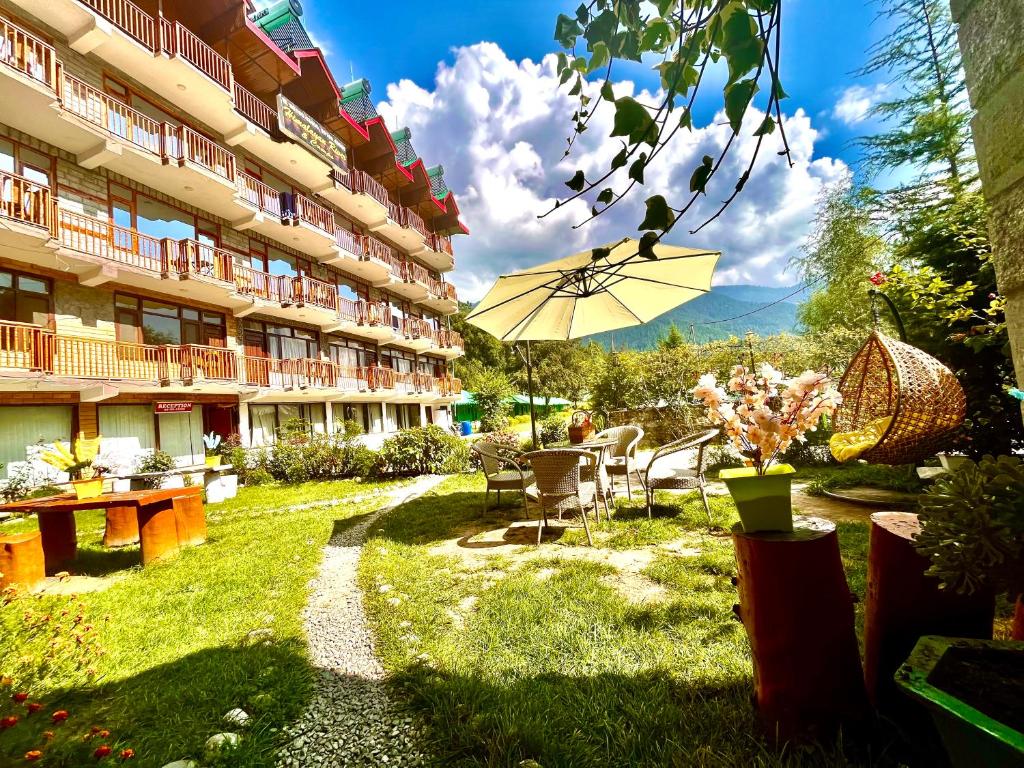 a courtyard of a hotel with a table and an umbrella at Himalayan Riverside Resort, Manali in Manāli