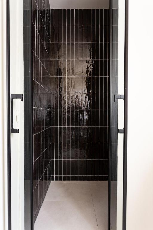 a glass shower door with black tiles in a bathroom at The Carla Suite Eiffel Tower View in Paris