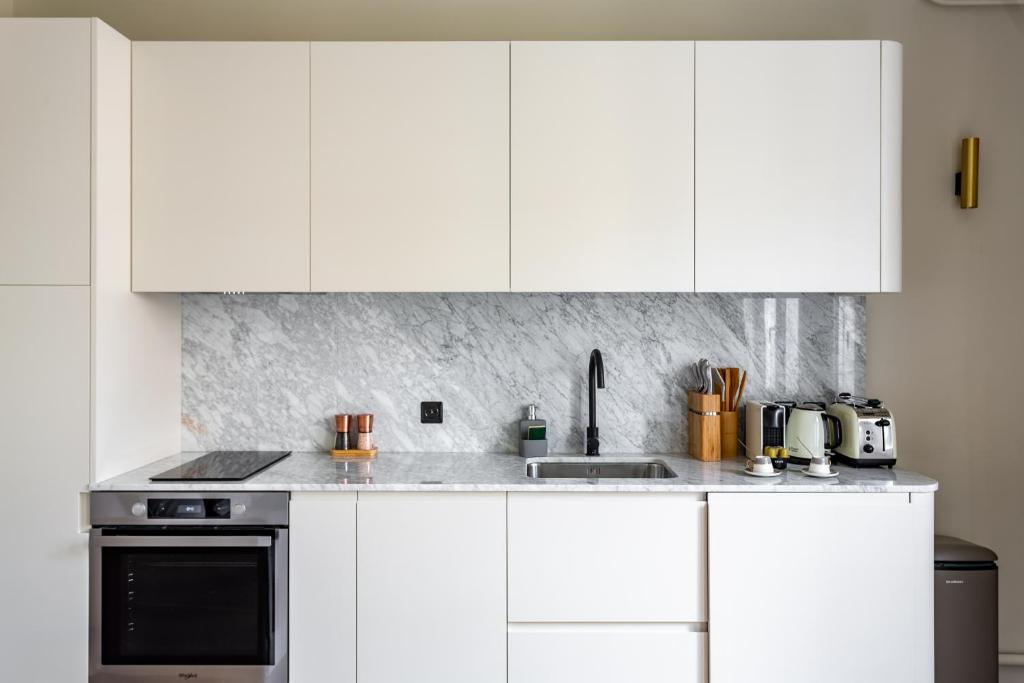 a white kitchen with white cabinets and a sink at The Carla Suite Eiffel Tower View in Paris