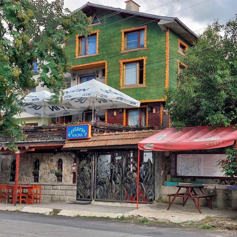 a building with a table and umbrellas in front of it at Семеен хотел Калина Family hotel Kalina Говедарци in Govedartsi