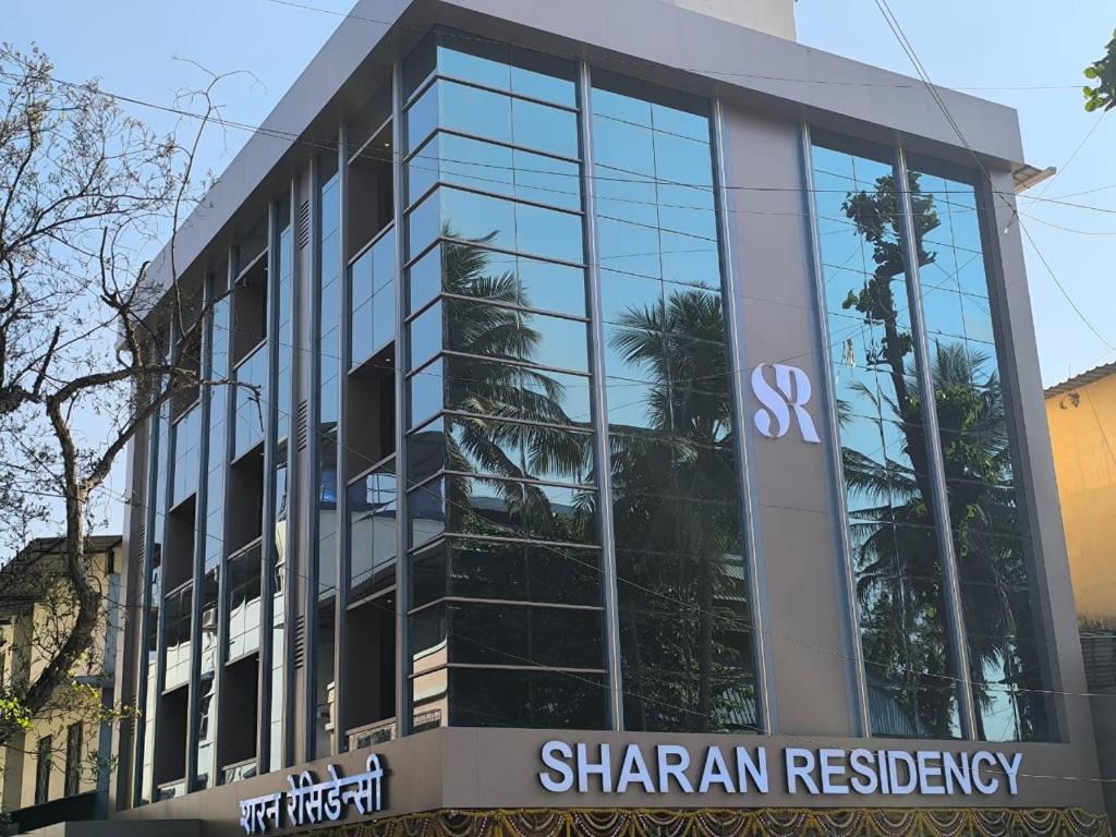 a glass building with a shan agency sign in front of it at Sharan Residency in Navi Mumbai