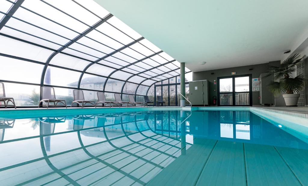 an indoor swimming pool with a glass ceiling at Kyriad Prestige Residence & Spa Cabourg-Dives-sur-Mer in Dives-sur-Mer