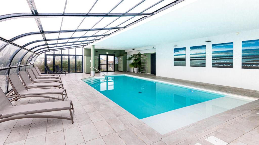 a swimming pool in a building with lounge chairs at Kyriad Prestige Residence & Spa Cabourg-Dives-sur-Mer in Dives-sur-Mer