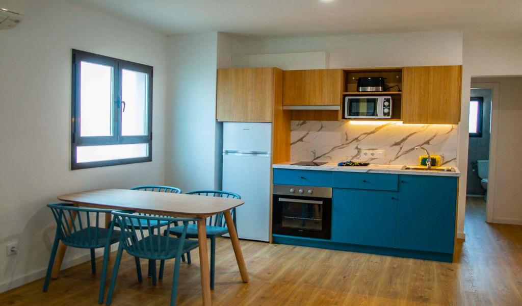 カラ・エン・ブラネスにあるApartamentos Sol y Mar IIのキッチン(青いキャビネット、テーブル、椅子付)