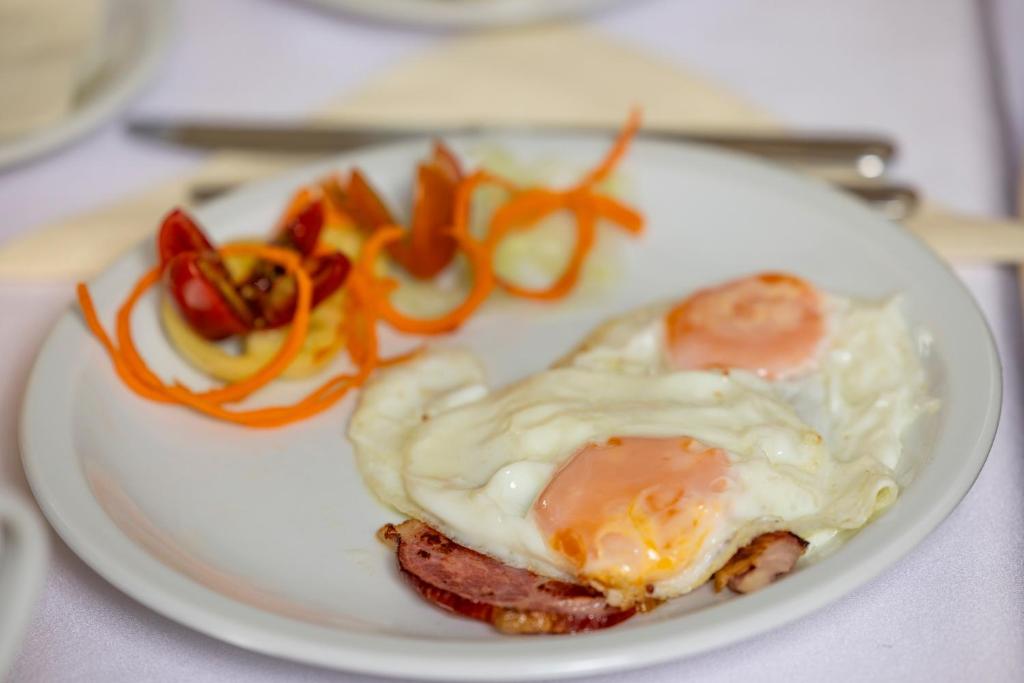 a white plate with an egg and bacon and vegetables at Pansion Maltar Varaždin in Varaždin