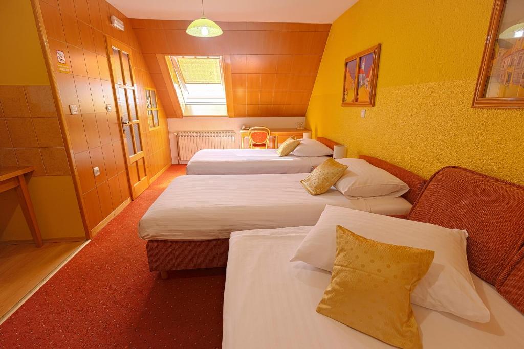 a hotel room with three beds with yellow walls at Pansion Maltar Varaždin in Varaždin