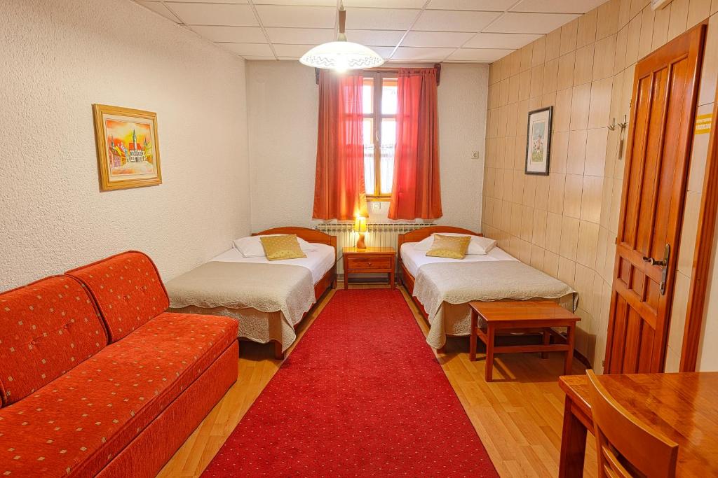 a room with two beds and a couch and a red rug at Pansion Maltar Varaždin in Varaždin