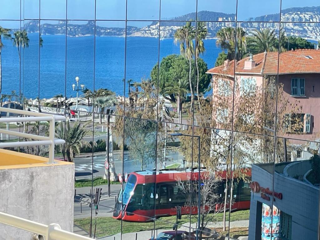 Ein roter Bus fährt eine Straße am Meer entlang. in der Unterkunft STUDIO SUR LA PROMENADE DES ANGLAIS AVEC VUE MER ORIGINALE À 40 m DE LA PLAGE in Nizza