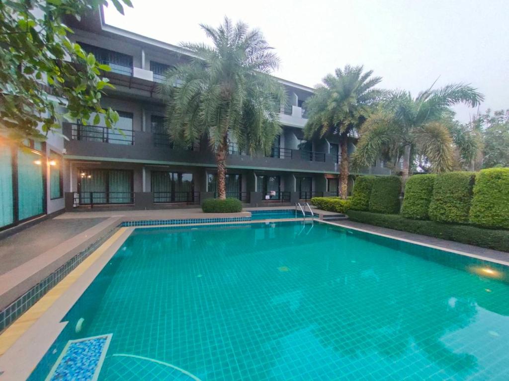 a swimming pool in front of a building with palm trees at Evergreen Resort Chanthaburi in Chanthaburi