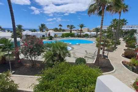 a resort with a swimming pool and palm trees at Precioso apartamento en Playa Bastián in Costa Teguise
