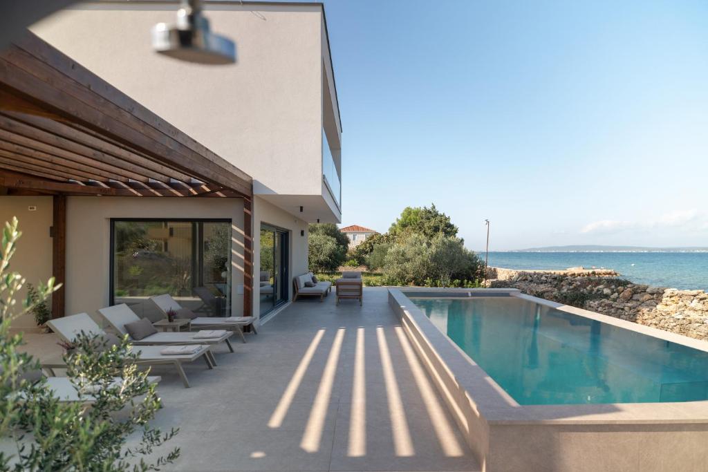 a house with a swimming pool next to the ocean at Courtside Luxury Villa Dalmatia in Dobropoljana