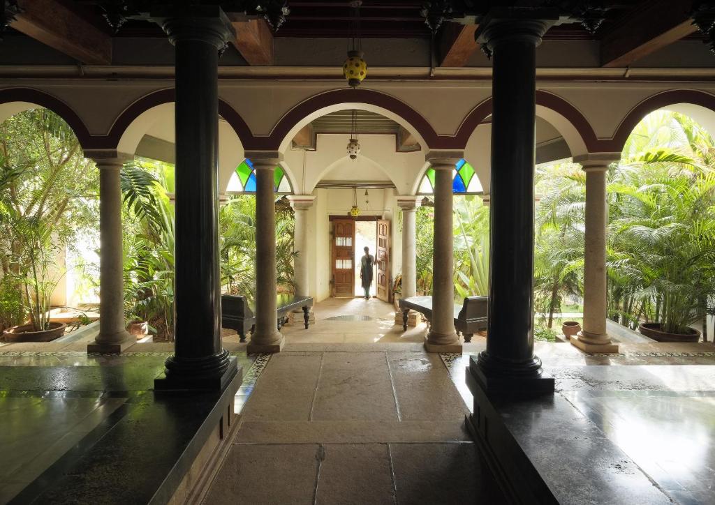 a building with columns and a hallway with trees at Saratha Vilas Chettinad in Kānādukāttān