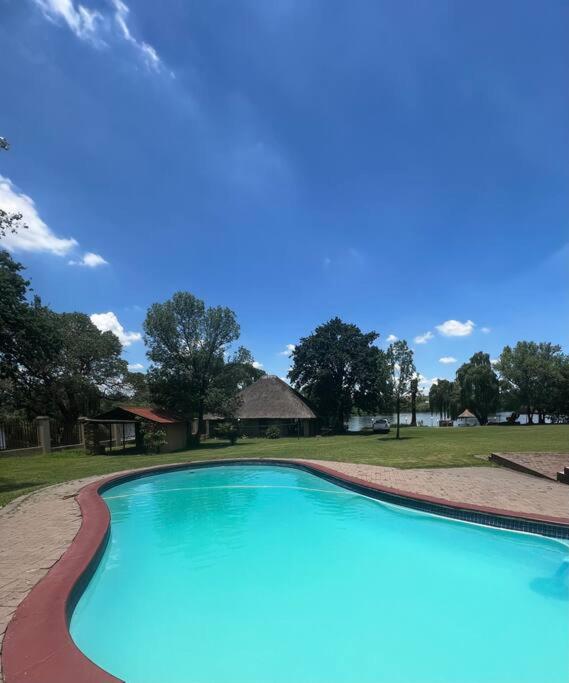 a large blue swimming pool with a house in the background at Vaal Haven - riverside getaway in Vanderbijlpark