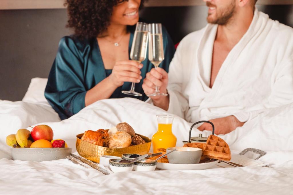 a man and a woman sitting in bed with wine glasses at Van Der Valk Sélys Liège Hotel &amp; Spa in Liège