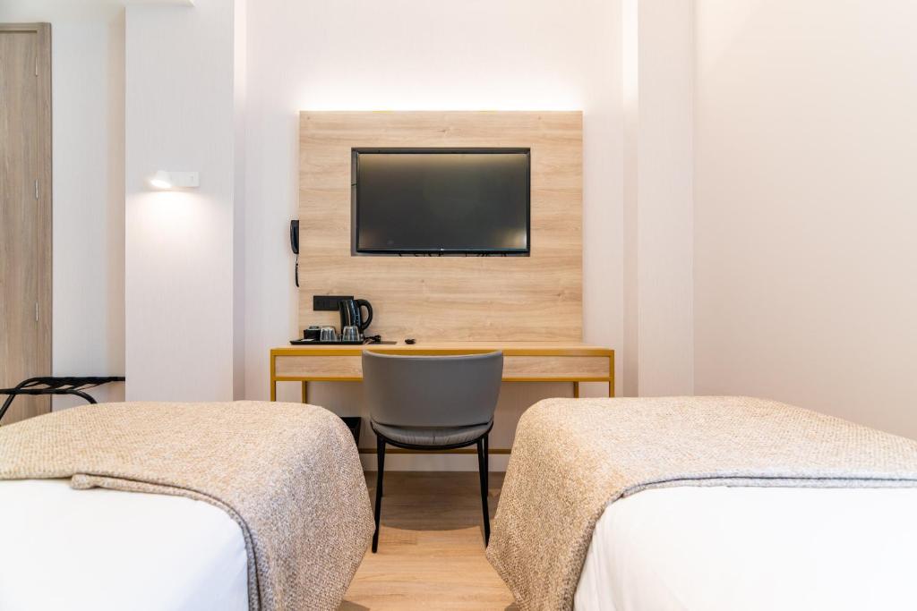 a room with two beds and a desk with a television at Hotel Málaga Vibes in Málaga