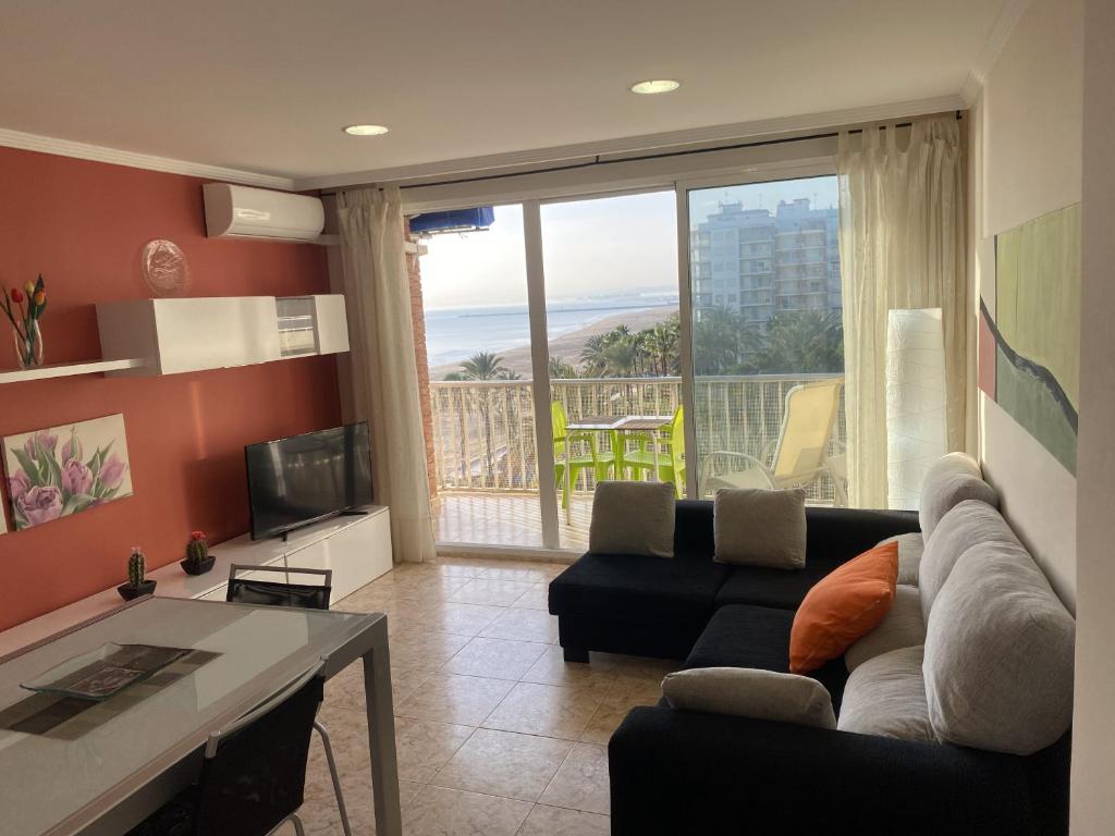 sala de estar con sofá, TV y balcón en Beachfront and Cozy Apartment, en Cullera
