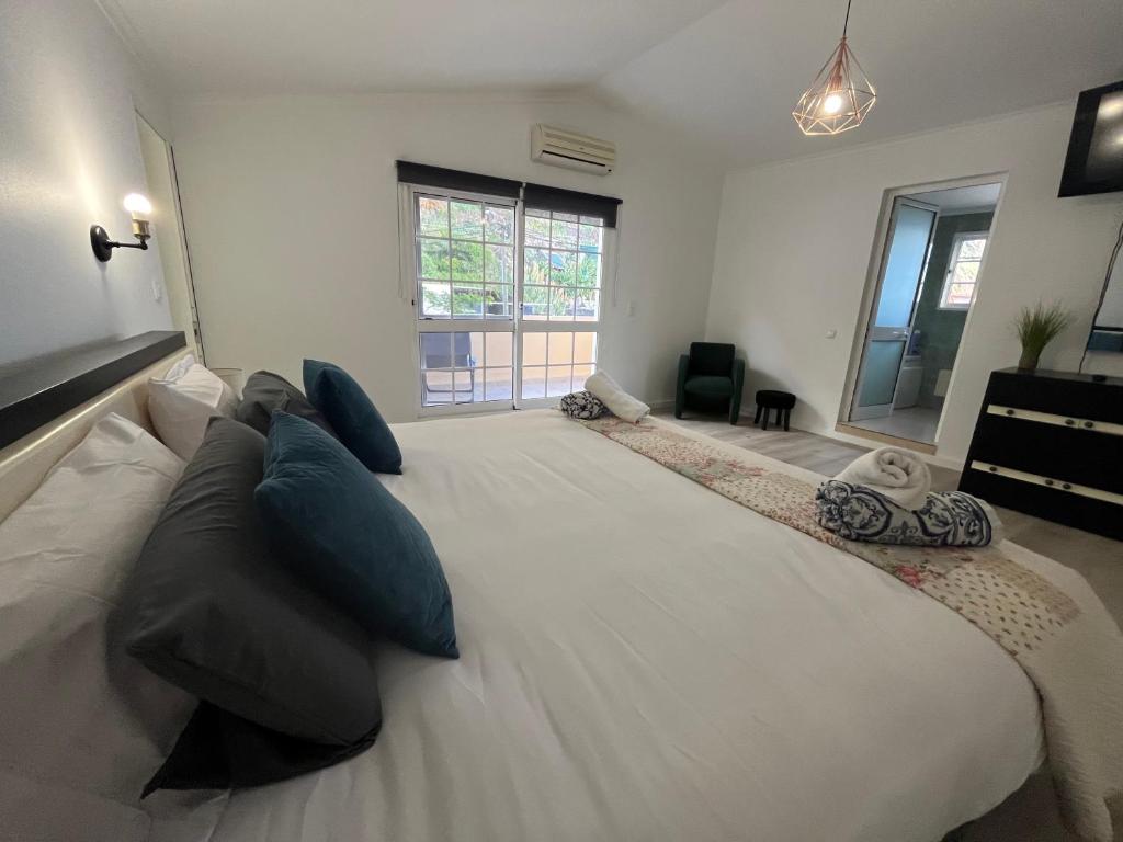 uma grande cama branca com almofadas azuis num quarto em villa com piscina entre o mar e as montanhas em Paul do Mar