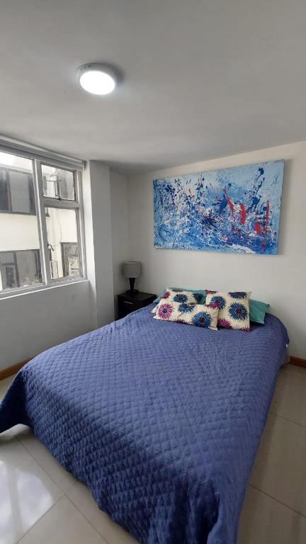 Un dormitorio con una cama azul con almohadas y una pintura en APARTAMENTO CHAPINERO CENTRAL, en Bogotá