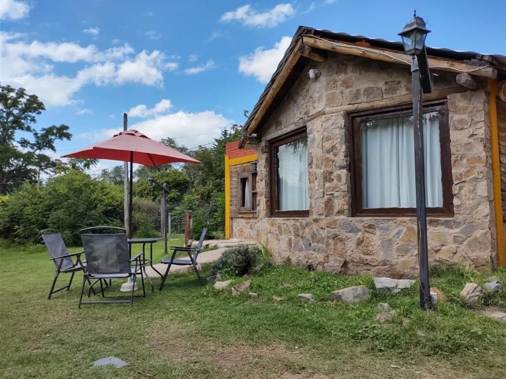 a stone cottage with a table and chairs and an umbrella at cabañas aromas de las sierras in El Volcán