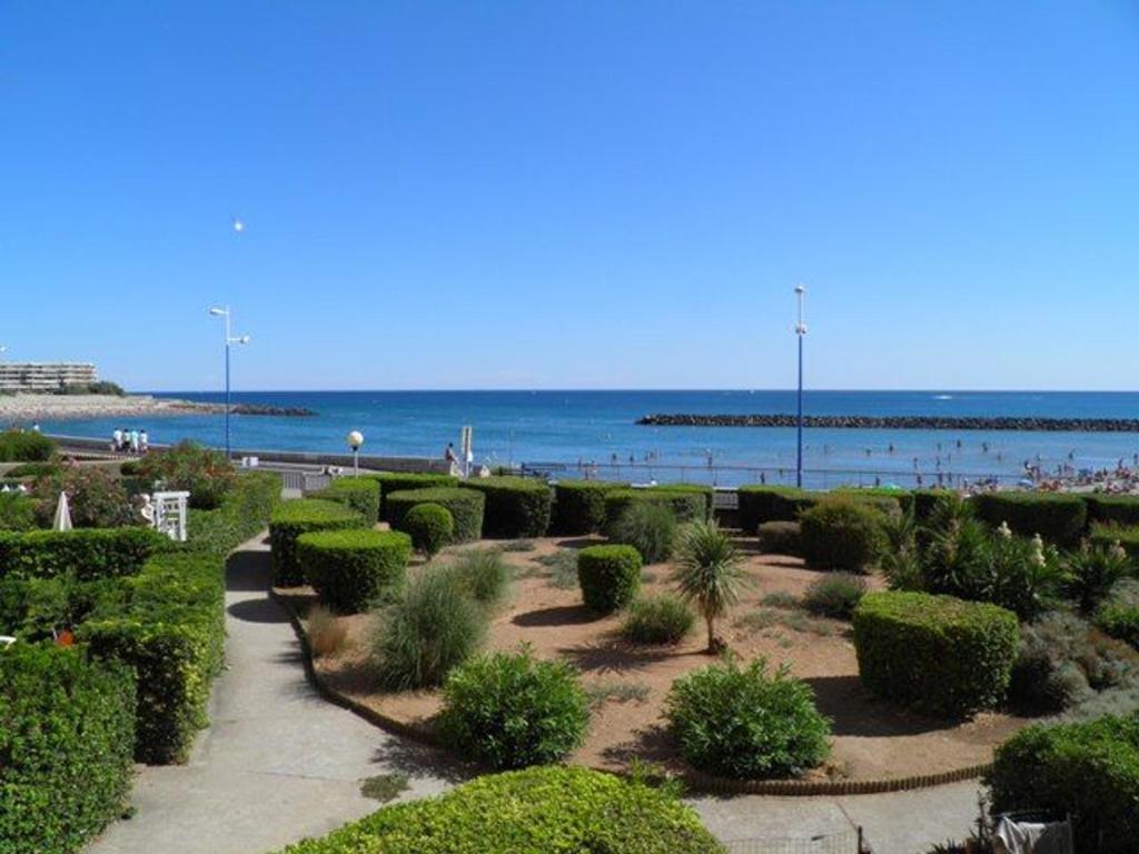 un jardin avec des buissons et une plage en arrière-plan dans l'établissement Appartement 2P rénové, vue mer, parking, plage en face - FR-1-338-530, à Sète