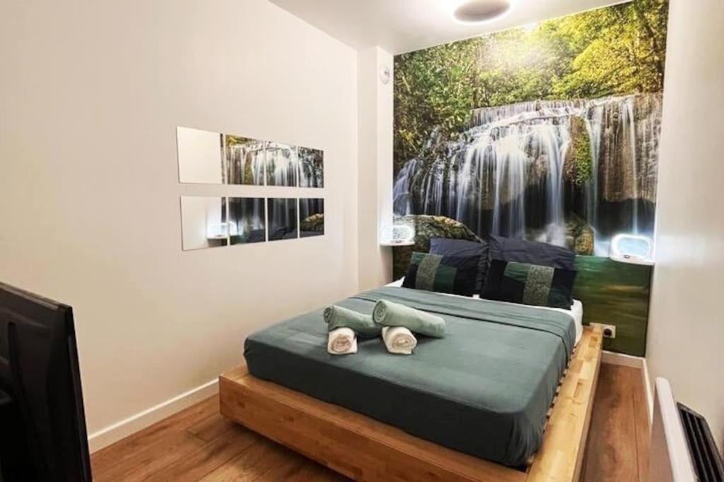 1 dormitorio con 1 cama con una pintura de cascada en la pared en Le petit cocon de Kintana -Disney-Parking, en Meaux