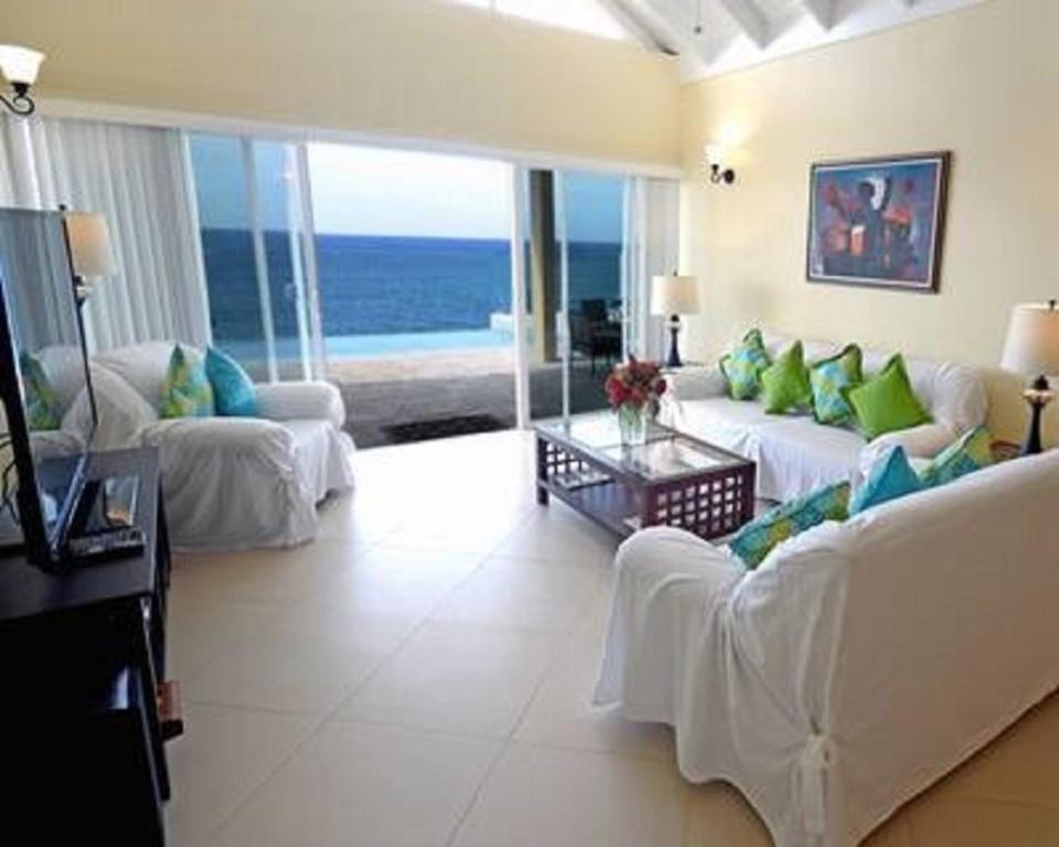 una sala de estar con muebles blancos y vistas al océano. en Je Suis Content - 4 Bed 4 B-r Beachfront Villa W-staff, en Duncans