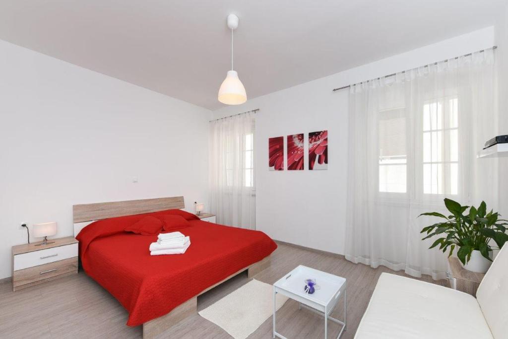 a white bedroom with a red bed and a table at Rooms Old Town in Zadar