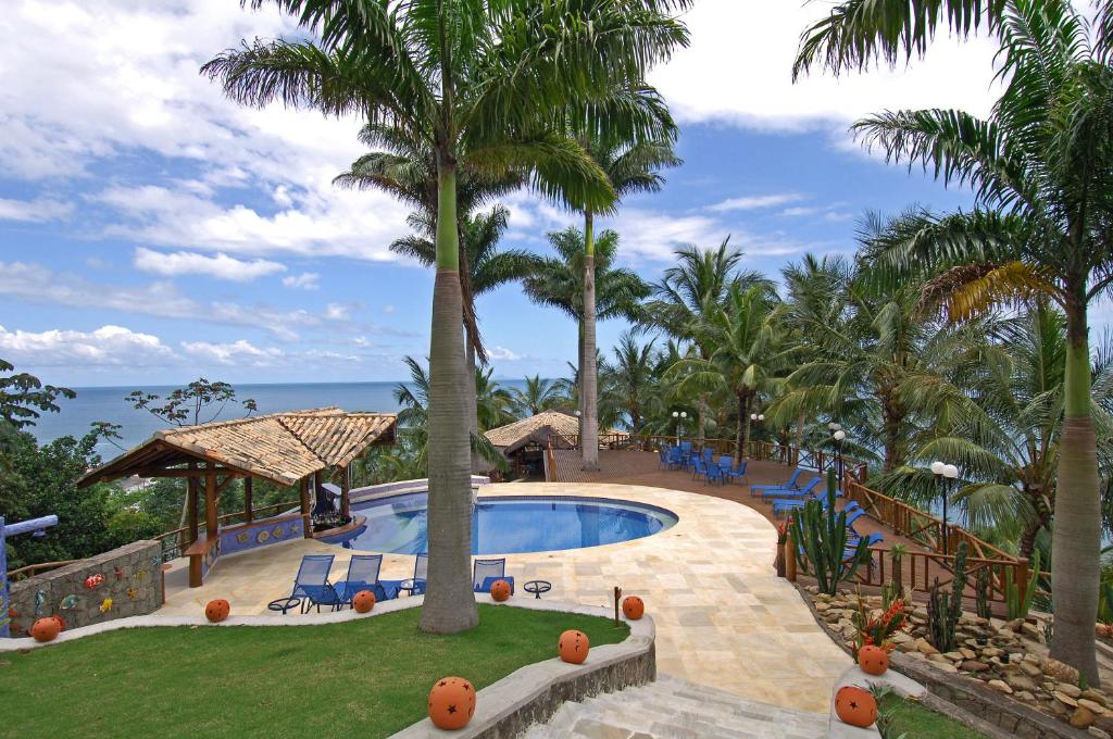 a resort swimming pool with palm trees and the ocean at Pousada Singuitta - Ilhabela in Ilhabela