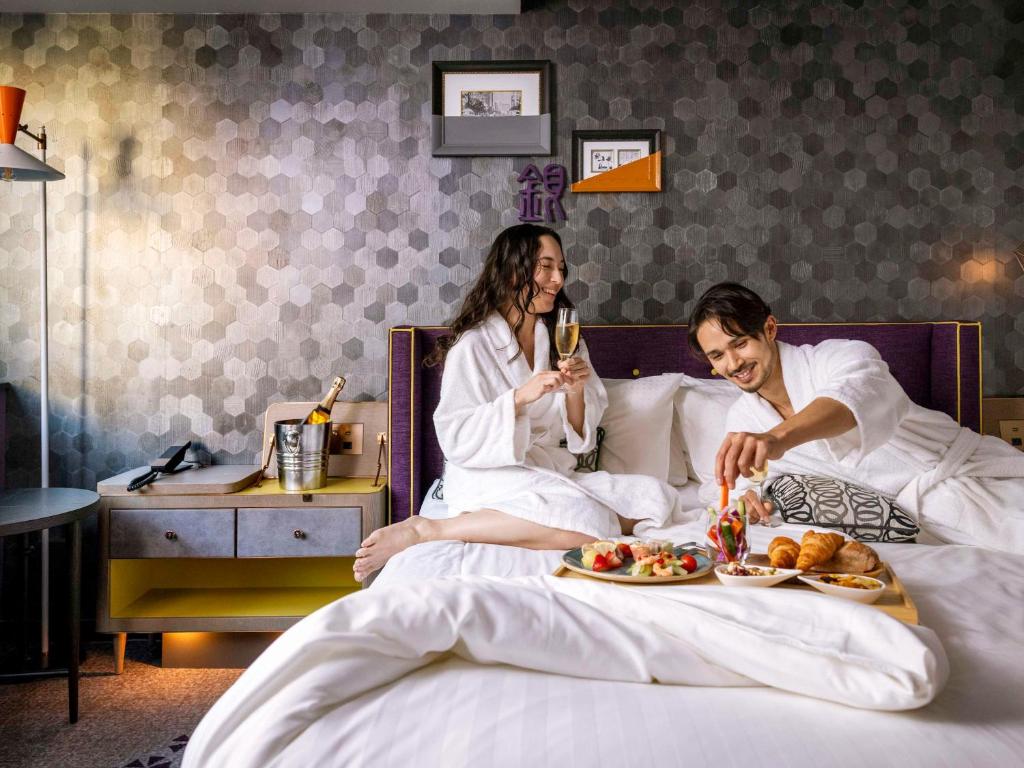 un homme et une femme assis au lit avec des assiettes de nourriture dans l'établissement Mercure Tokyo Ginza, à Tokyo