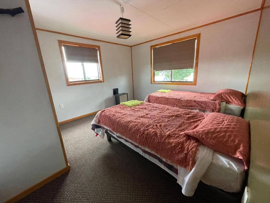 a bedroom with two beds and two windows at Posada De Los Gatos in Puerto Natales
