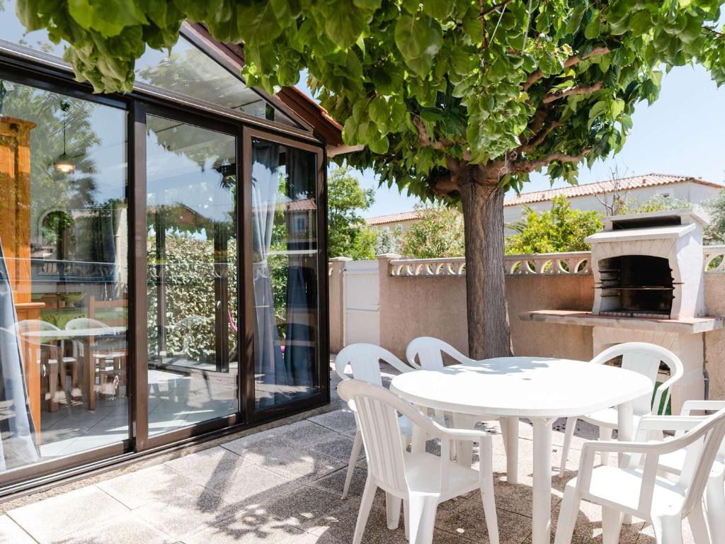une table et des chaises blanches sur une terrasse avec un arbre dans l'établissement Pavillon familial 3 pièces + mezzanine, climatisé, proche plage, Narbonne-Plage - FR-1-409-91, à Narbonne-Plage