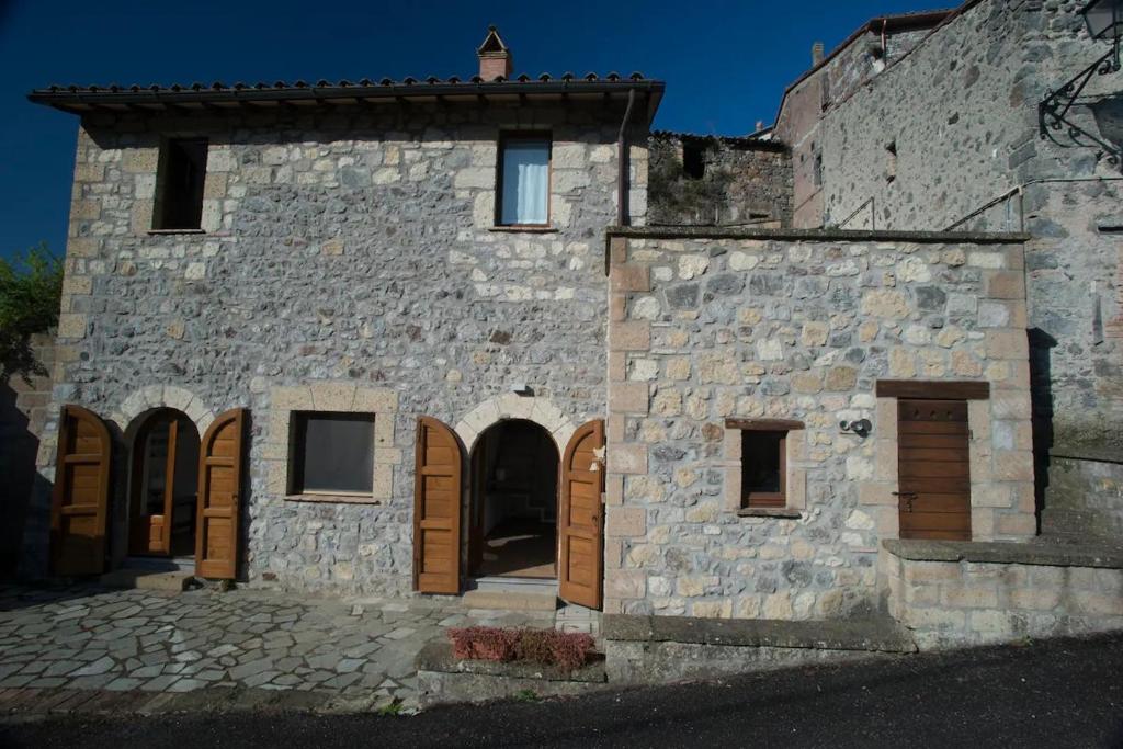 un antiguo edificio de piedra con puertas y ventanas de madera en Le Terrazze della Tuscia, en Latera