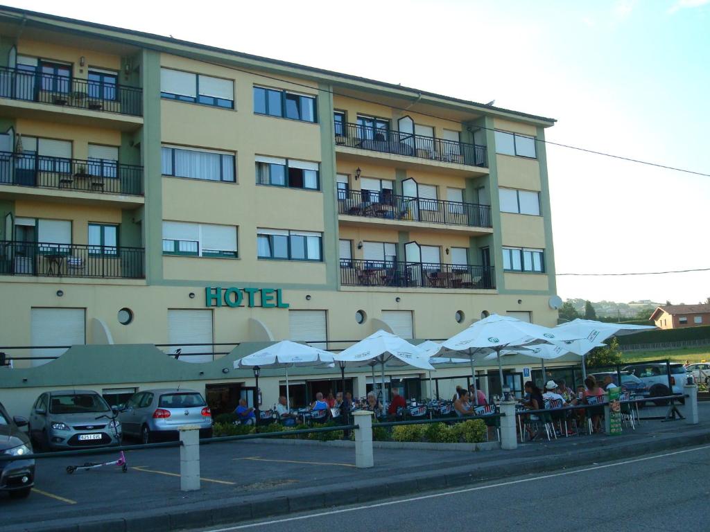 un hotel con mesas y sombrillas delante en Hotel Brisamar en Bañugues